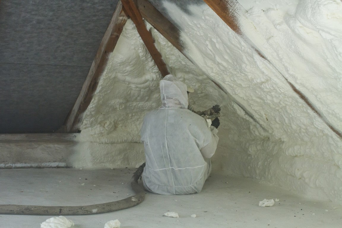 A person applying spray foam insulation in the attic